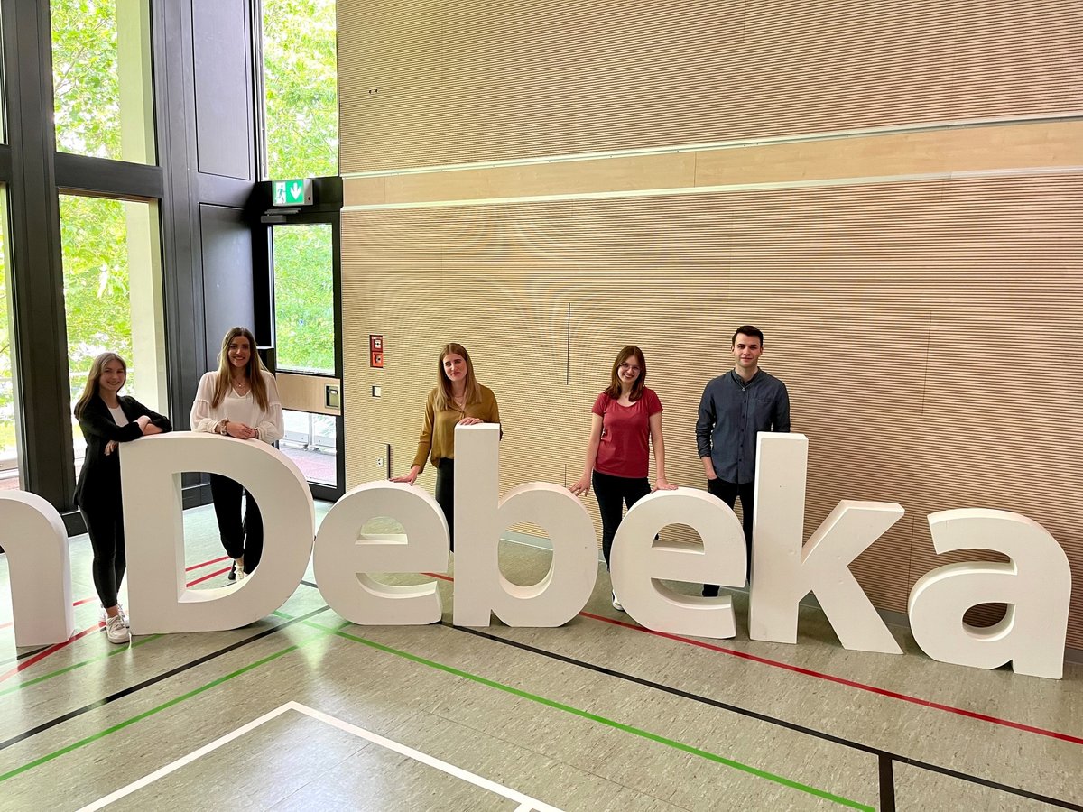 Fünf junge Menschen stehen vor hinter einem Schild mit der Auschrift "Debeka"