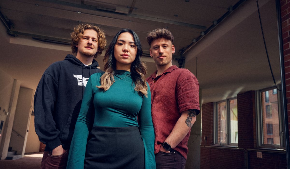 Tom, Cam und Noel sind Botschafter für die Ausbildung. Alle drei schauen in die Kamera. Sie stehen in einen Raum, der etwas dunkel ist. Der Fokus liegt auf den Azubis.