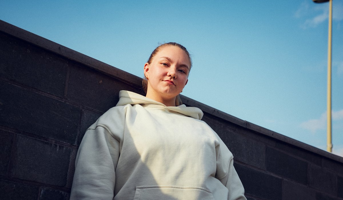 Astrid ist Botschafterin für die Ausbildung. Der IHK Azubi Kampagne könnenlernen. Sie steht draußen vor einer Wand und trägt einen weißen Pullover. 