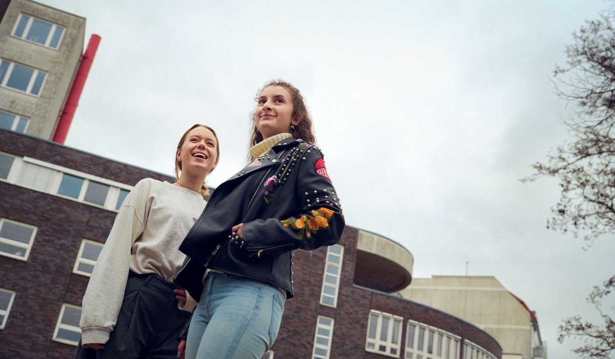 Mahalia und Meret sind Botschafterinnen für die Ausbildung. Meret trägt einen weißen Pullover und hat blondes Haar, sie lächelt. Mahalia hat braune Locken und trägt eine schwarze Lederjacke.