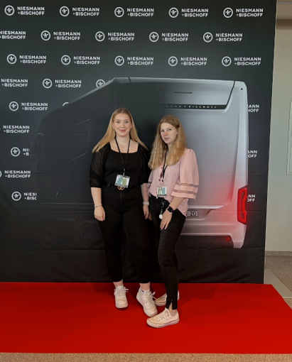 Zwei junge Frauen stehen vor einer Logo-Wand